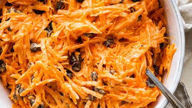 A carrot raisin salad in a white bowl with a spoon.