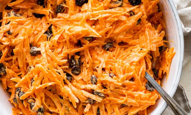 A carrot raisin salad in a white bowl with a spoon.