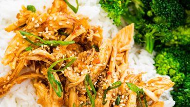 Slow cooker teriyaki chicken served on a plate with white rice and broccoli. The chicken is topped with sesame seeds and green onions.