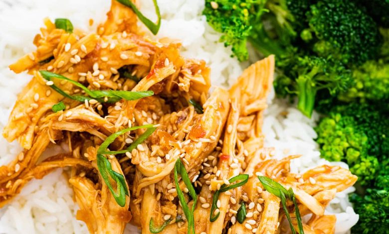 Slow cooker teriyaki chicken served on a plate with white rice and broccoli. The chicken is topped with sesame seeds and green onions.