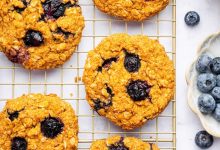 Six sweet potato blueberry oatmeal cookies on a wire cooling rack. Fresh blueberries are scattered next to the rack.