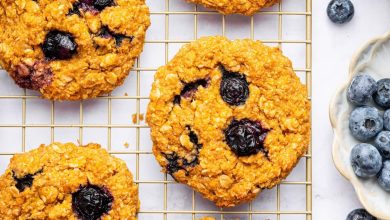 Six sweet potato blueberry oatmeal cookies on a wire cooling rack. Fresh blueberries are scattered next to the rack.