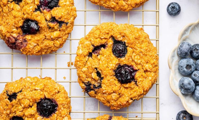 Six sweet potato blueberry oatmeal cookies on a wire cooling rack. Fresh blueberries are scattered next to the rack.