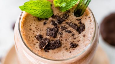 One mint chocolate protein shake in a glass topped with crushed Thin Mint cookies and fresh mint. There is a green straw in the glass.