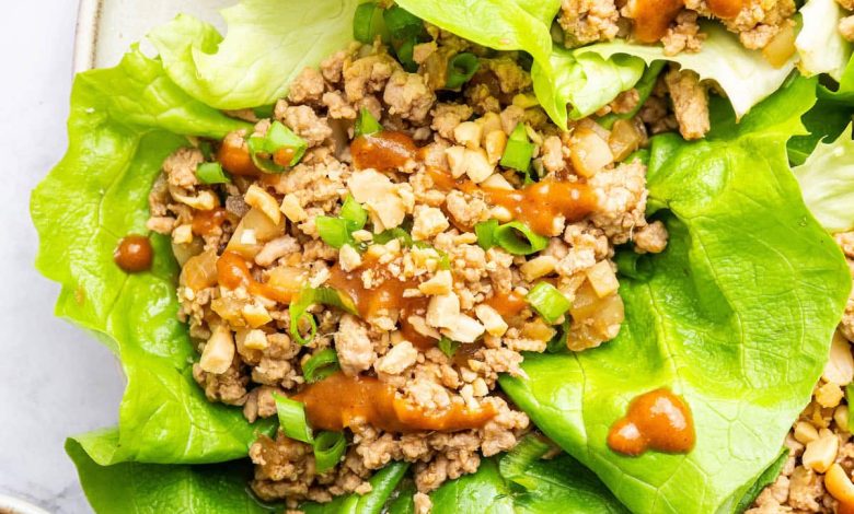 Ground chicken lettuce wraps served on a plate with a peanut sauce drizzle and fresh green onions.