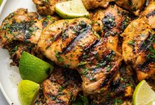 Cooked cilantro lime chicken thighs served on a plate topped with fresh cilantro and lime wedges.