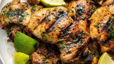 Cooked cilantro lime chicken thighs served on a plate topped with fresh cilantro and lime wedges.