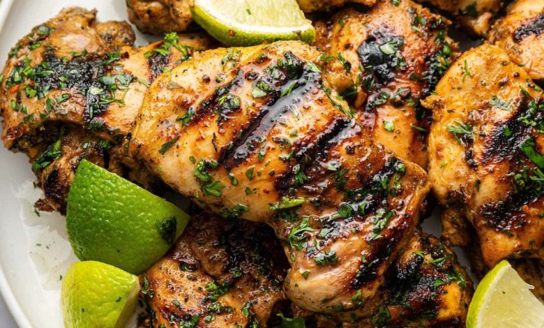 Cooked cilantro lime chicken thighs served on a plate topped with fresh cilantro and lime wedges.