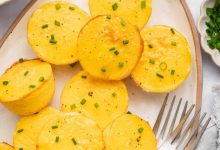 12 cottage cheese egg bites on a white serving plate topped with chopped chives. There are two forks on the plate.