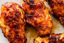 Four grilled BBQ chicken breasts on a white serving plate.