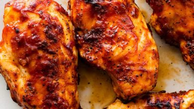 Four grilled BBQ chicken breasts on a white serving plate.