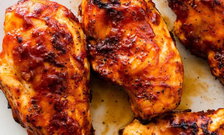 Four grilled BBQ chicken breasts on a white serving plate.