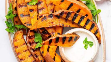 Grilled sweet potatoes on a serving platter topped with fresh parsley and served with a side of garlic aioli. There is one sweet potato dipped in the aioli.