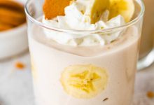 High-protein banana pudding in a glass topped with whipped cream, sliced bananas and a wafer cookie.