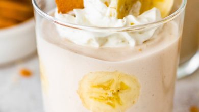 High-protein banana pudding in a glass topped with whipped cream, sliced bananas and a wafer cookie.
