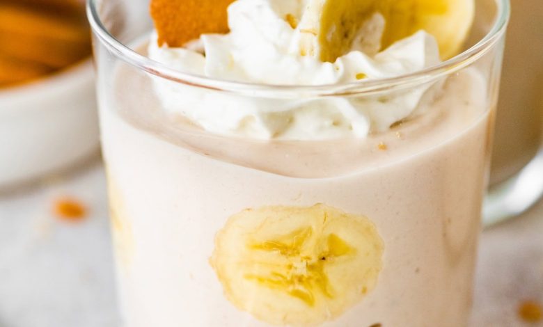 High-protein banana pudding in a glass topped with whipped cream, sliced bananas and a wafer cookie.