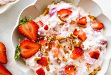 A bowl of strawberry pretzel salad topped with strawberries and crushed pretzels.