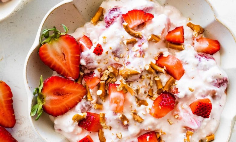 A bowl of strawberry pretzel salad topped with strawberries and crushed pretzels.