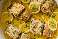 4 Mahi mahi fillets in a skillet with a lemon butter garlic sauce. There are lemon slices in the skillet and everything is topped with fresh parsley.