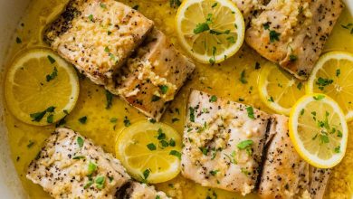 4 Mahi mahi fillets in a skillet with a lemon butter garlic sauce. There are lemon slices in the skillet and everything is topped with fresh parsley.