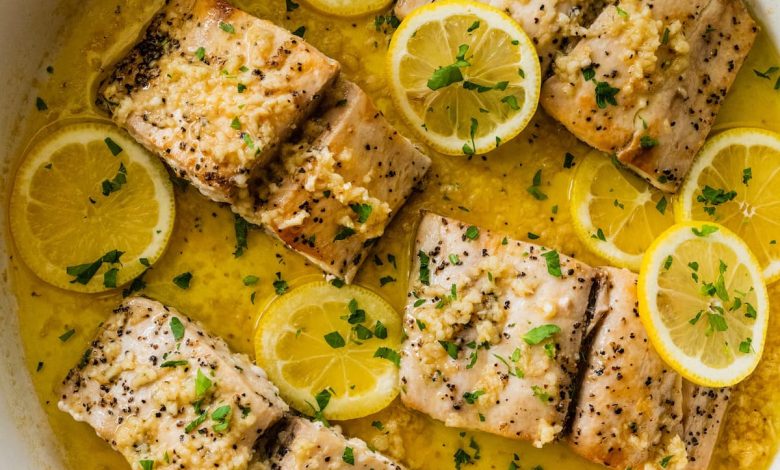 4 Mahi mahi fillets in a skillet with a lemon butter garlic sauce. There are lemon slices in the skillet and everything is topped with fresh parsley.