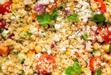 A mixed quinoa chickpea salad with tomatoes, cucumbers, feta, and parsley, in a white bowl.