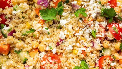 A mixed quinoa chickpea salad with tomatoes, cucumbers, feta, and parsley, in a white bowl.