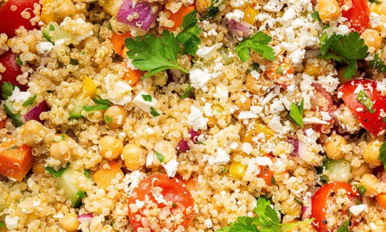 A mixed quinoa chickpea salad with tomatoes, cucumbers, feta, and parsley, in a white bowl.