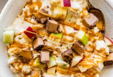 A snickers salad protein bowl topped with apple chunks, a chopped protein bar and a drizzle of peanut butter.