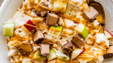 A snickers salad protein bowl topped with apple chunks, a chopped protein bar and a drizzle of peanut butter.