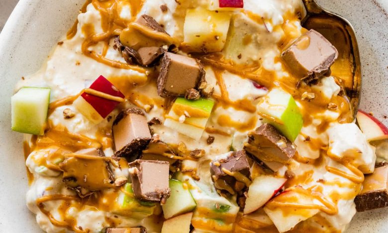 A snickers salad protein bowl topped with apple chunks, a chopped protein bar and a drizzle of peanut butter.