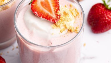 One glass filled with high-protein strawberry mousse topped with a dollop of cocowhip, one halved fresh strawberry and crushed graham crackers.