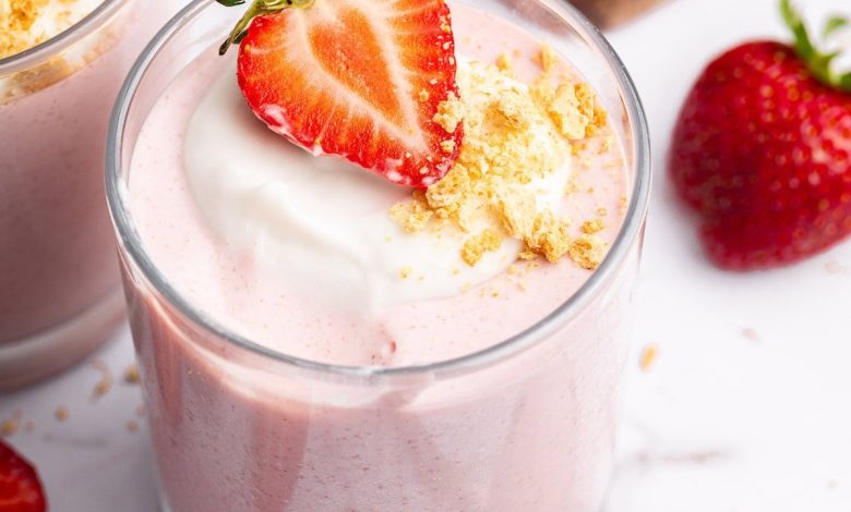One glass filled with high-protein strawberry mousse topped with a dollop of cocowhip, one halved fresh strawberry and crushed graham crackers.