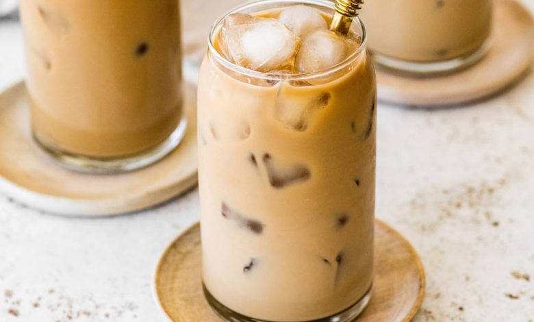 A glass of iced coffee with milk fully mixed in, served on a small wooden plate with a metal straw.