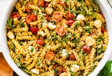A serving bowl filled with caprese pasta salad. There are serving spoons next to the bowl.
