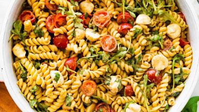 A serving bowl filled with caprese pasta salad. There are serving spoons next to the bowl.