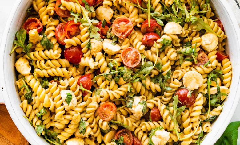 A serving bowl filled with caprese pasta salad. There are serving spoons next to the bowl.