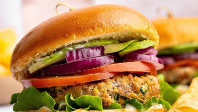 A chicken burger served on a brioche bun topped with lettuce, tomato, red onion and avocado. The burger is served with a side of potato chips.
