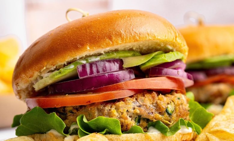 A chicken burger served on a brioche bun topped with lettuce, tomato, red onion and avocado. The burger is served with a side of potato chips.