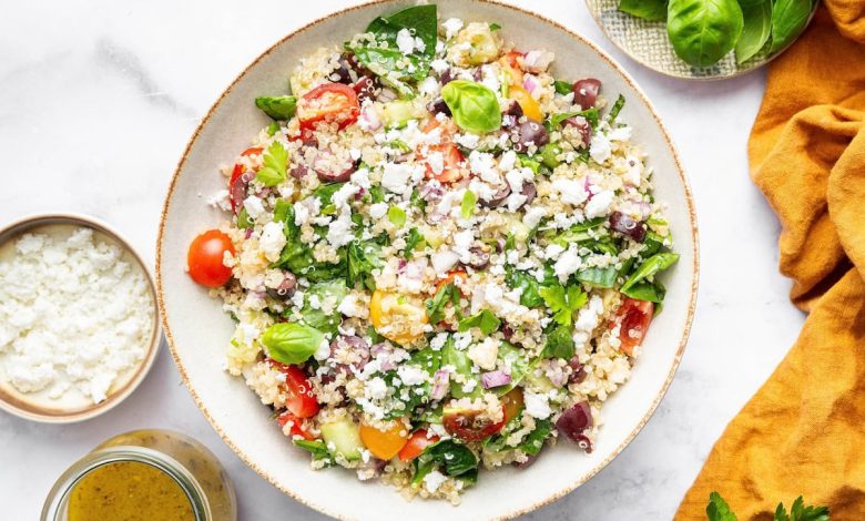 Greek quinoa salad in a tan serving bowl topped with crumbled feta cheese.