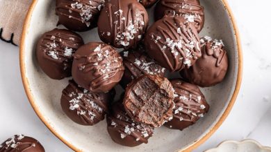 Bowl of chocolate protein balls stacked with flaky sea salt on top and one bitten into.