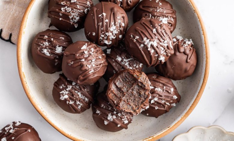 Bowl of chocolate protein balls stacked with flaky sea salt on top and one bitten into.