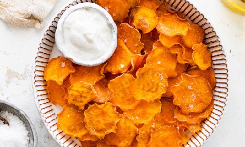 Baked sweet potato chips in a bowl with a small bowl of white dipping sauce.